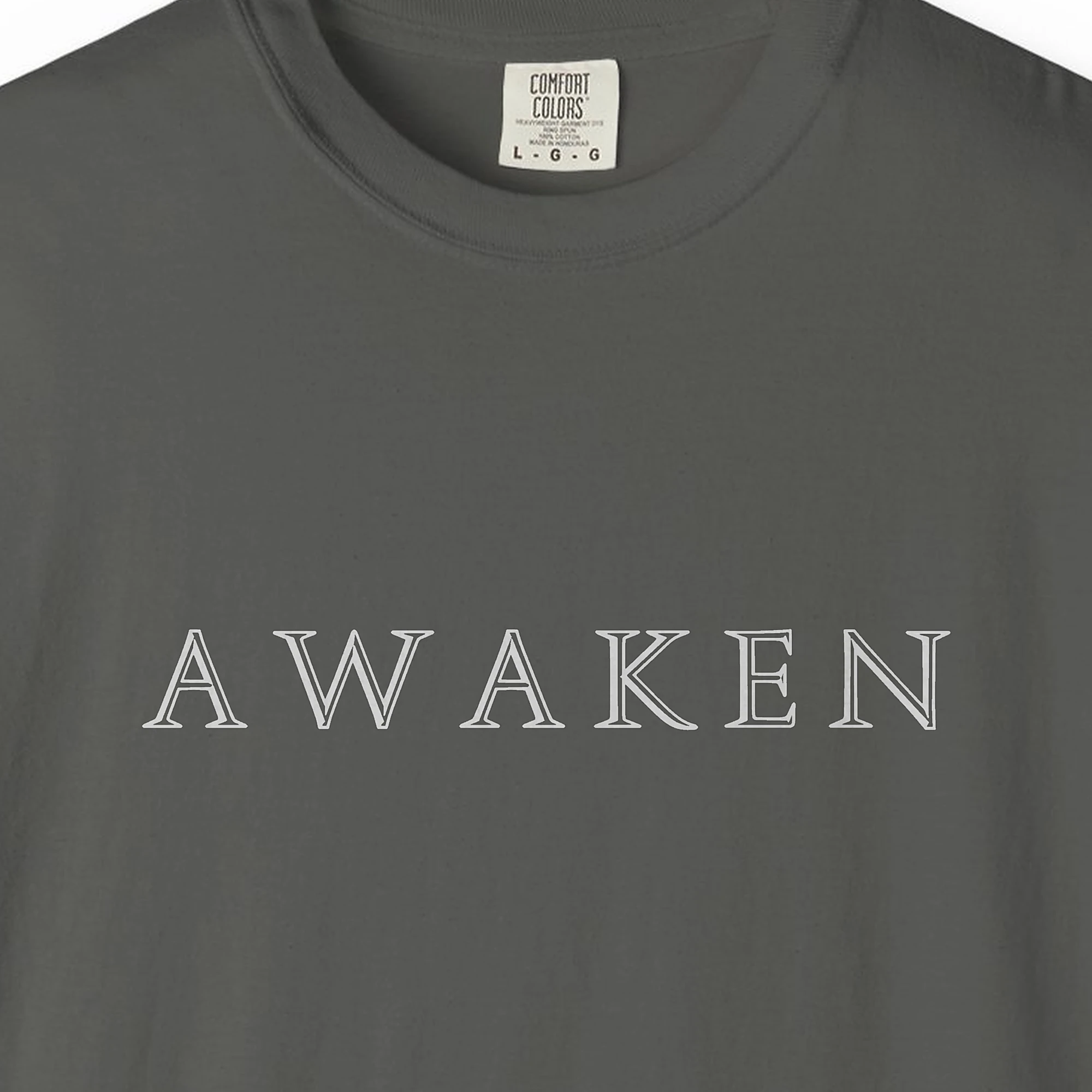 Close-up of the Awaken Engraved Capitals print on a Pepper Comfort Colors 1717 tee