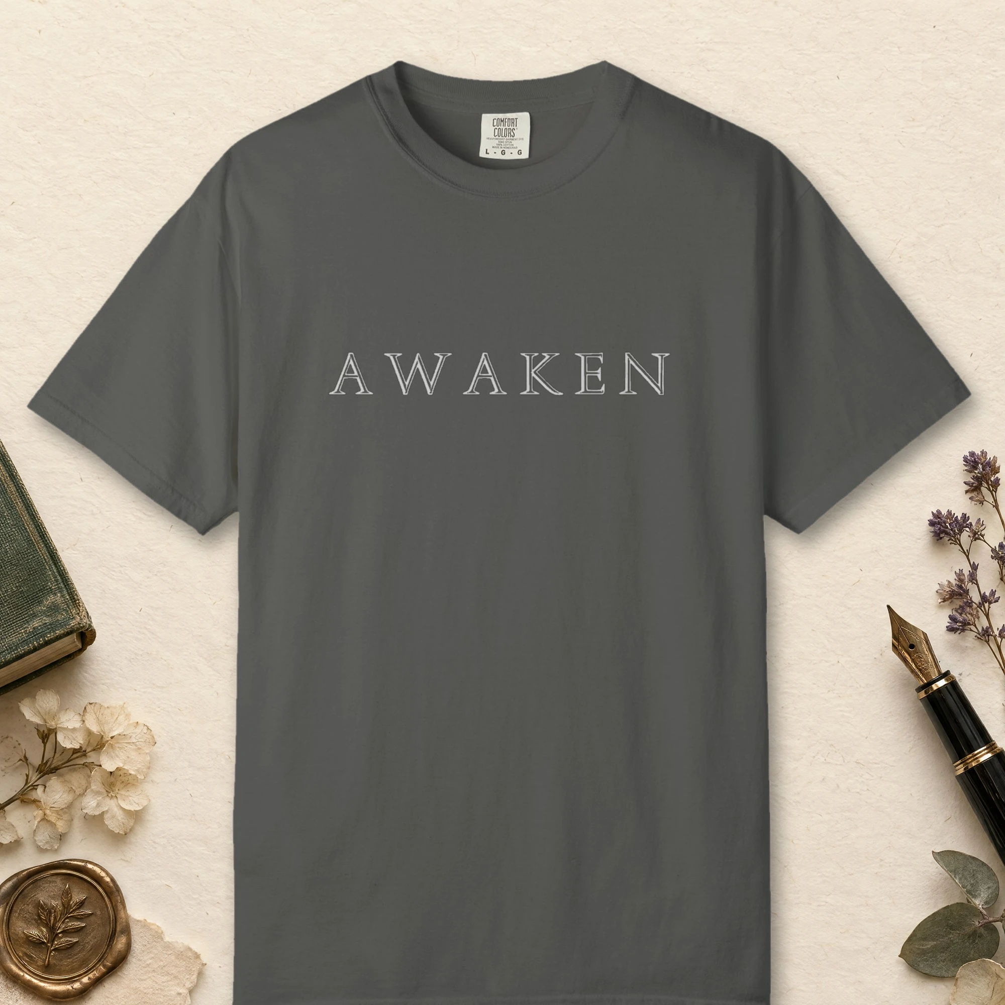 Awaken Engraved Capitals design on a Pepper Comfort Colors 1717 tee, laid flat