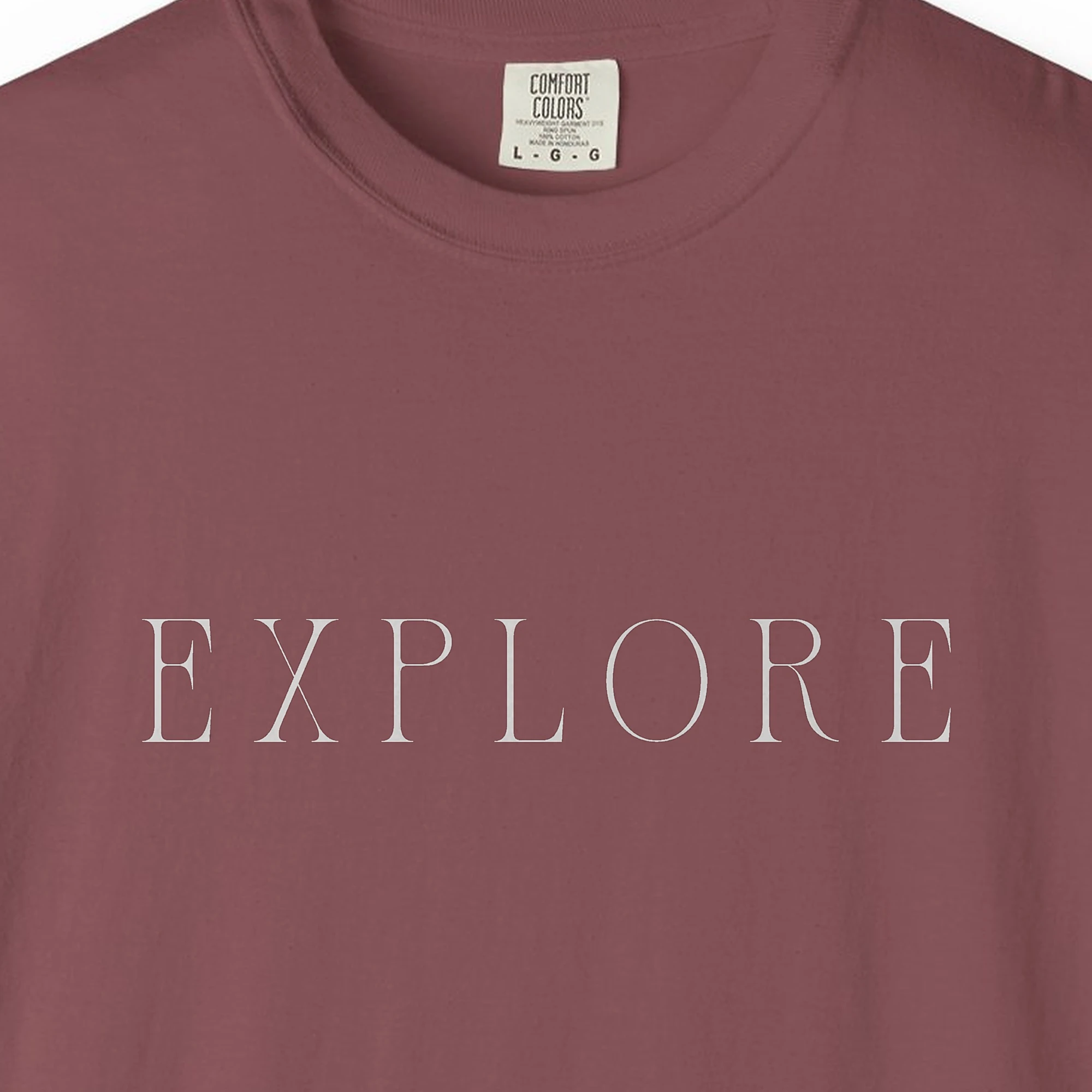 Close-up of the Explore Roman Capitals print on a Brick Comfort Colors 1717 tee