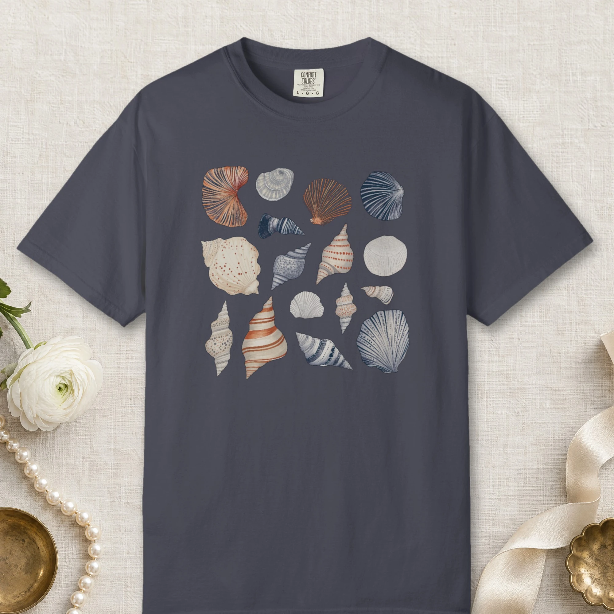 Gathered Seashells design on a Navy Comfort Colors 1717 tee, laid flat