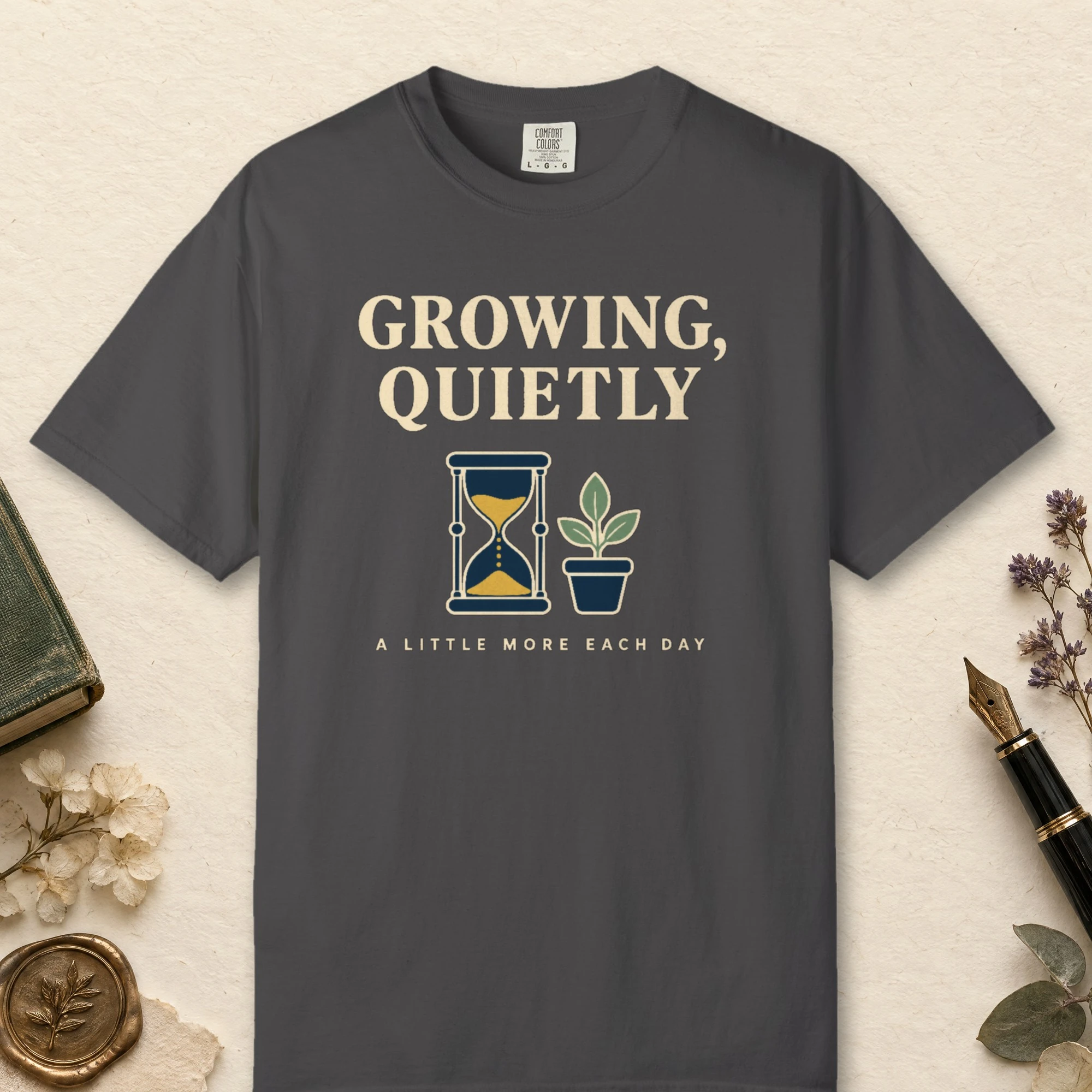 Growing Quietly design on a Graphite Comfort Colors 1717 tee, laid flat