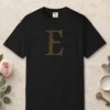 Initial E design on a Black Comfort Colors 1717 tee, laid flat
