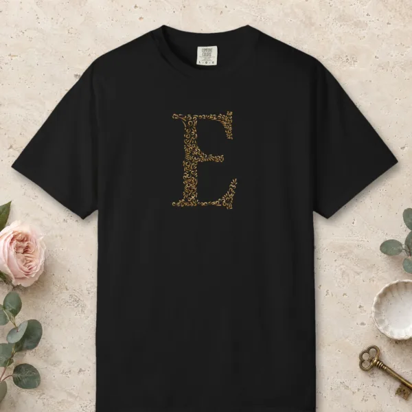 Initial E design on a Black Comfort Colors 1717 tee, laid flat