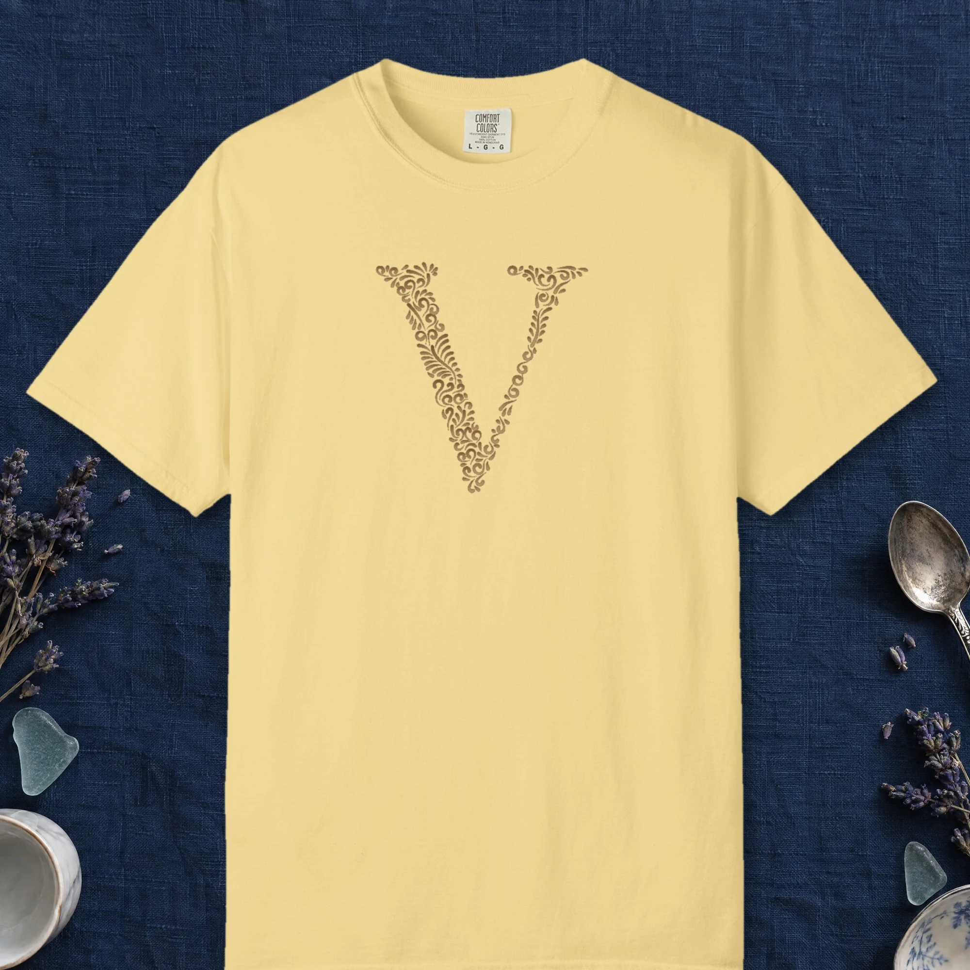 Initial V design on a Butter Comfort Colors 1717 tee, laid flat