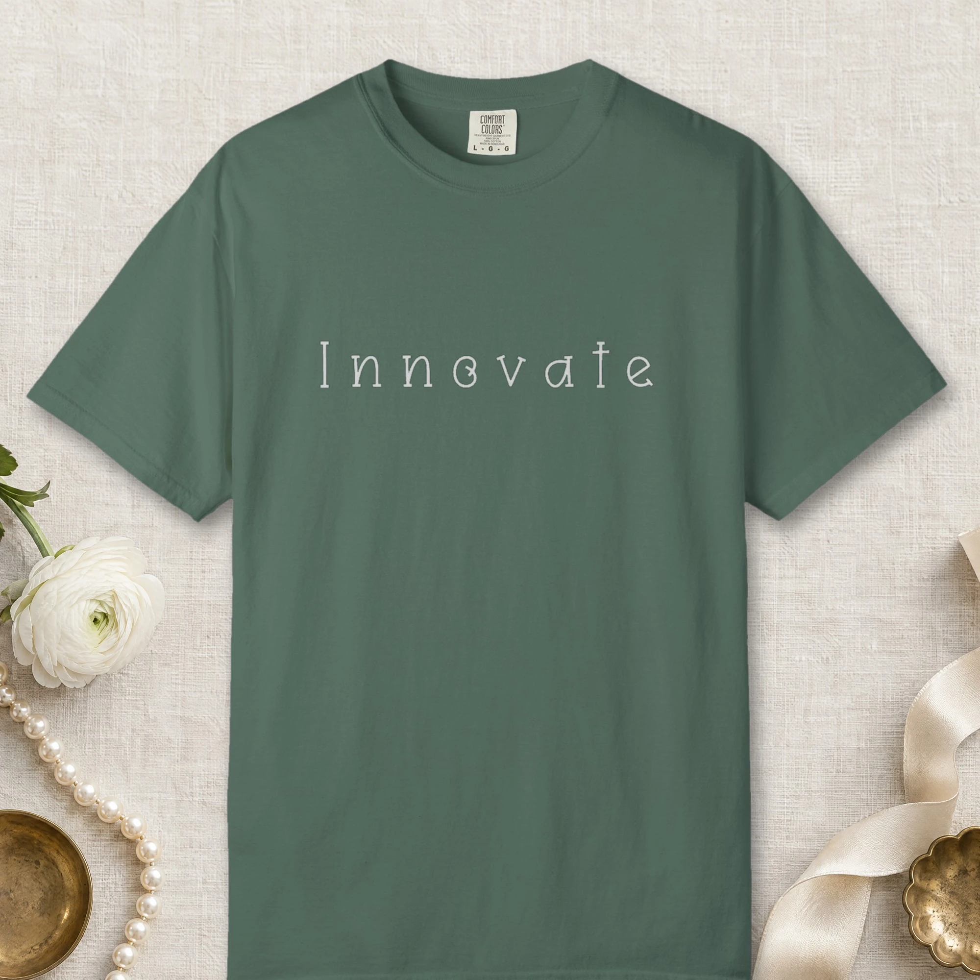 Innovate Curled Serif design on a Blue Spruce Comfort Colors 1717 tee, laid flat