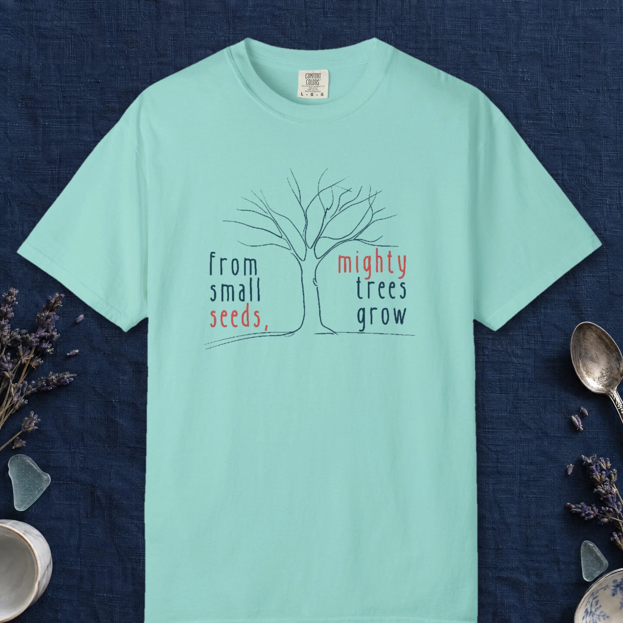 Mighty Trees Grow design on a Chalky Mint Comfort Colors 1717 tee, laid flat