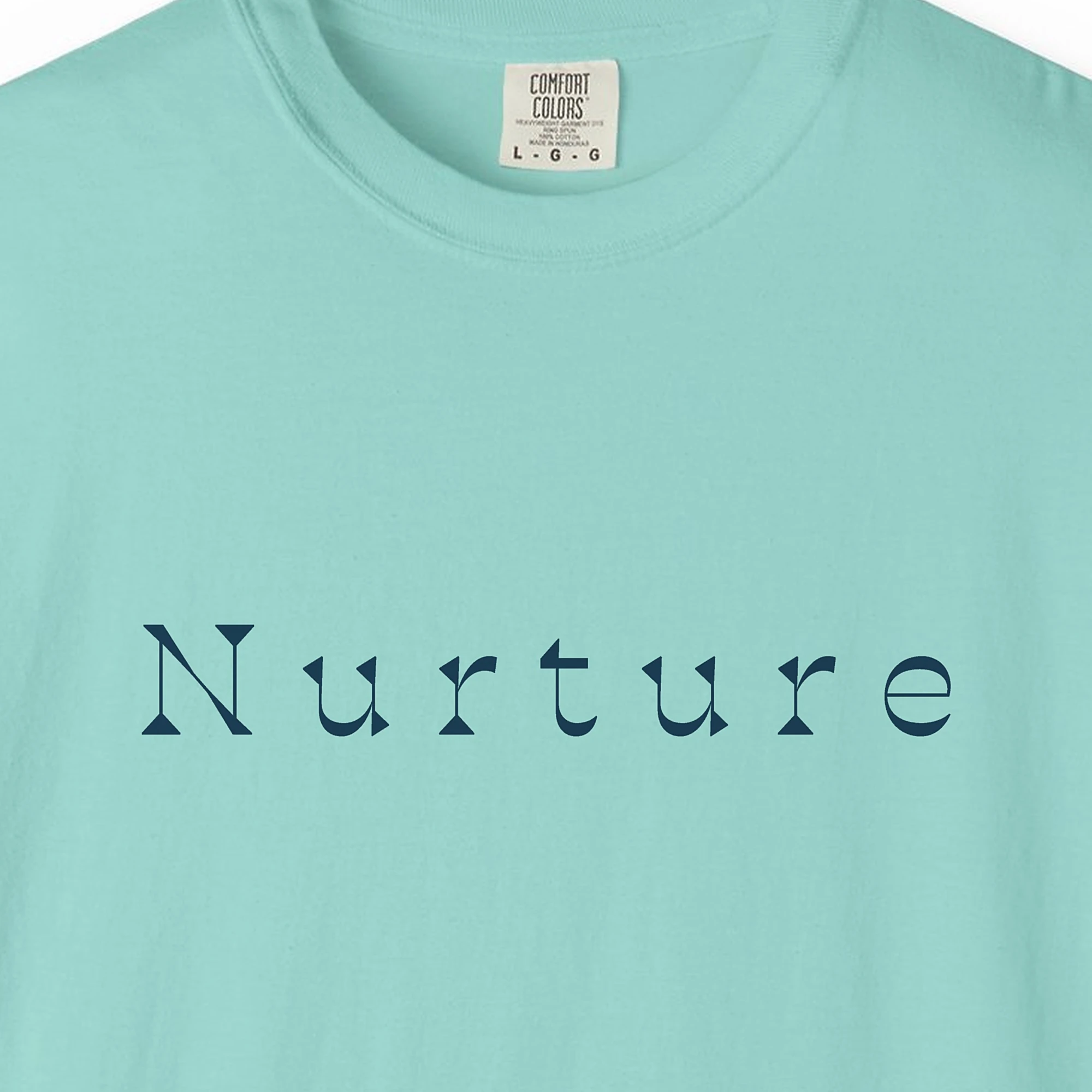Close-up of the Nurture Flared Serif print on a Chalky Mint Comfort Colors 1717 tee