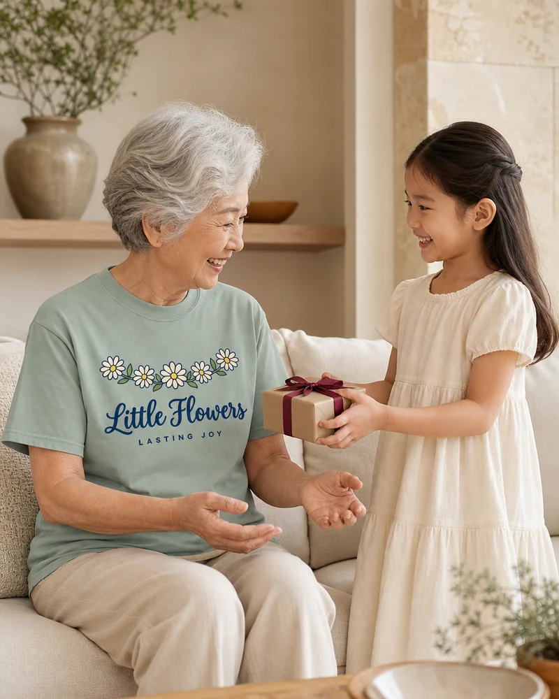 A grandmother receiving a small gift from her granddaughter (the grandmother in the Little Flowers Lasting Joy Tee in Bay)