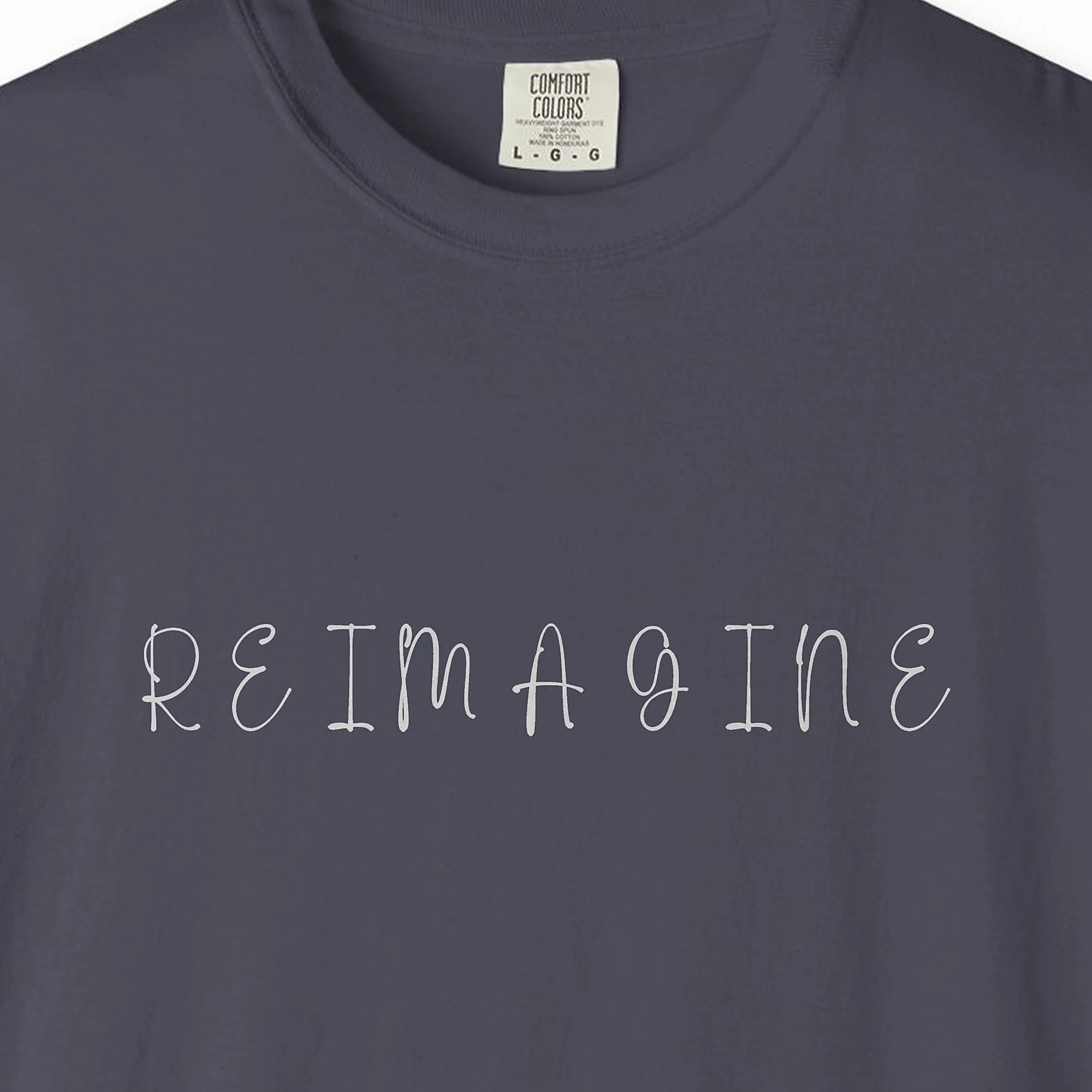 Close-up of the Reimagine Handwritten Capitals print on a Navy Comfort Colors 1717 tee