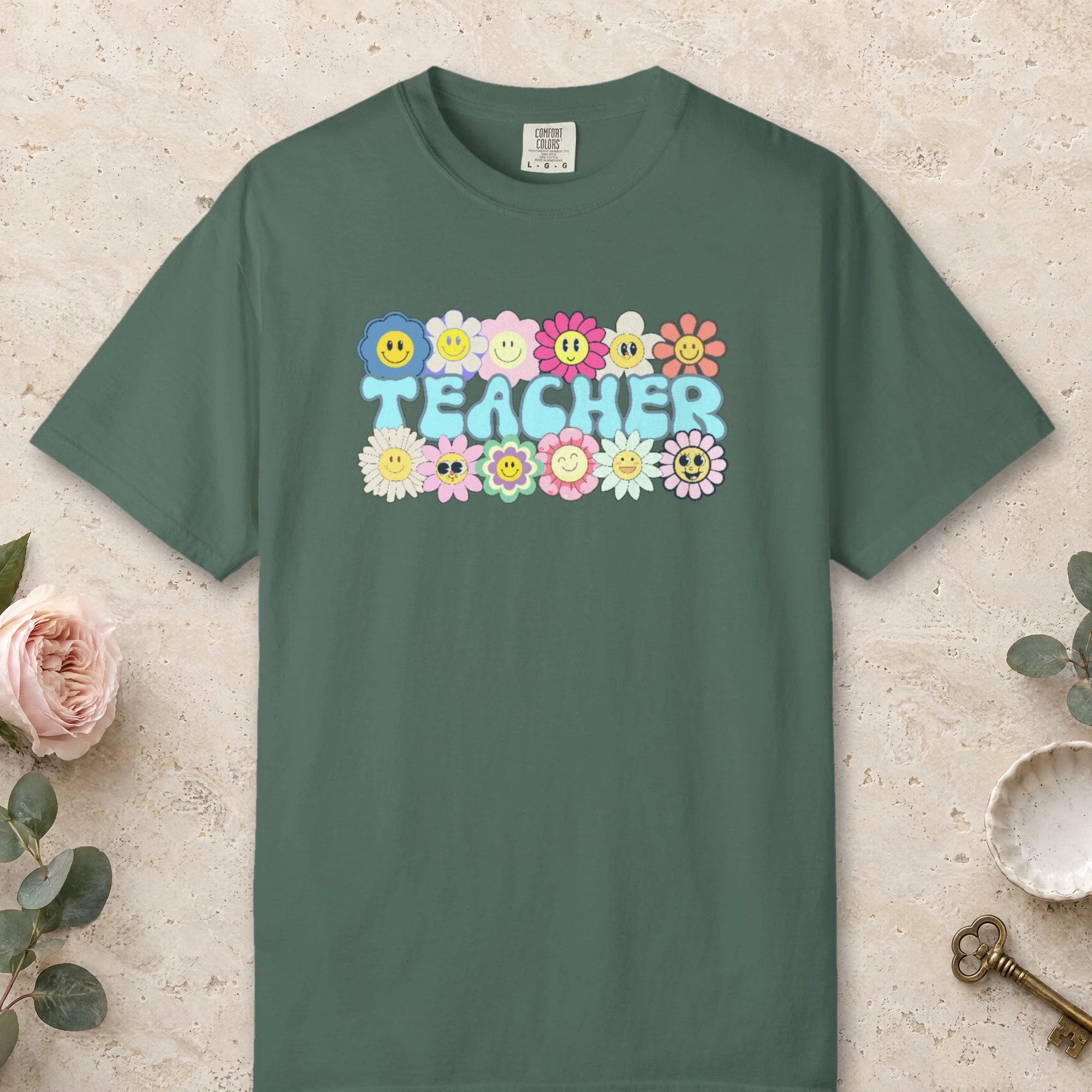 Smiling Daisies Teacher design on a Blue Spruce Comfort Colors 1717 tee, laid flat