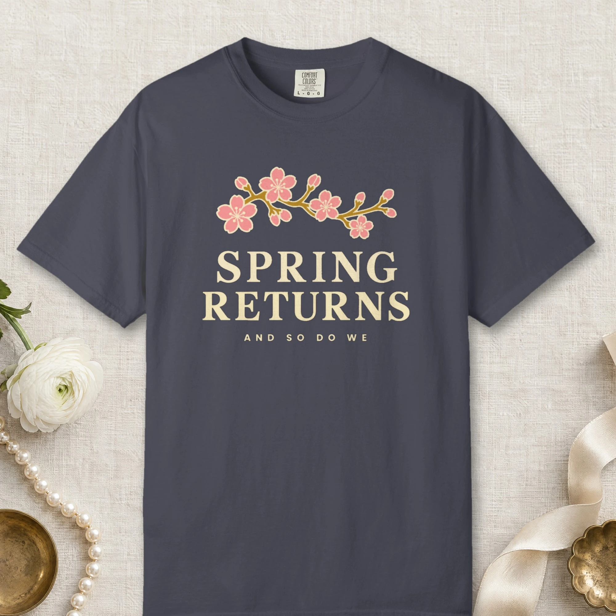 Spring Returns design on a Navy Comfort Colors 1717 tee, laid flat