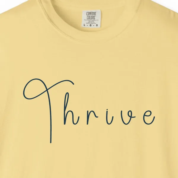 Close-up of the Thrive Handwritten print on a Butter Comfort Colors 1717 tee